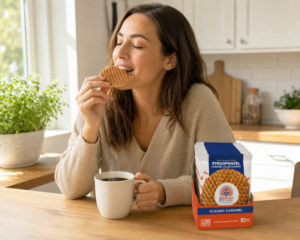Woman eating a 3 Bros Classic Caramel stroopwafel with coffee in a sunlit kitchen